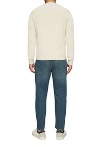 Sweatshirt couleur crème avec des poignets et un ourlet côtelés, porté avec un jean bleu foncé et des baskets blanches, montrant une tenue décontractée vue de dos.