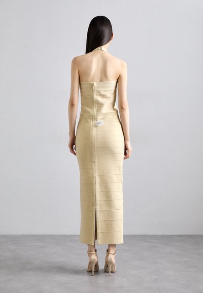 Robe dorée sans bretelles avec une silhouette ajustée, finition texturée et fermeture éclair au dos. Dispose d'une fente latérale et d'une étiquette placée à la taille.