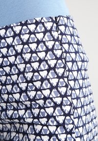 Blå och vit mönstrad tyg med trianglar och hjärtformer, med en sidoglittring vid plaggets kant. Slät textur.