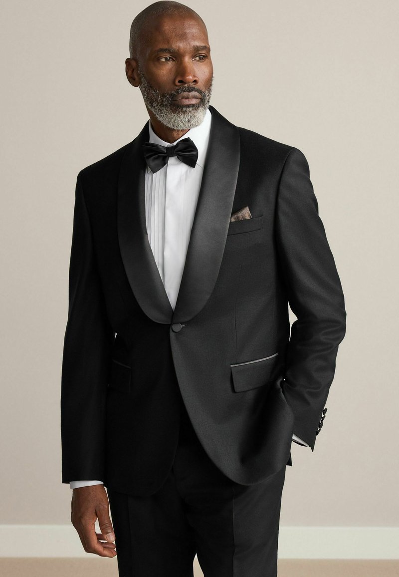 Black tuxedo with satin lapels, white pleated shirt, and black bow tie. Features a pocket square and tailored fit with subtle accents.