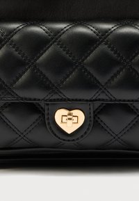 Μαύρη τσάντα χειρός από δερμάτινο καπιτονέ υλικό με χρυσαφένιο κούμπωμα σε σχήμα καρδιάς, με εμφανείς ραφές και απαλή υφή.