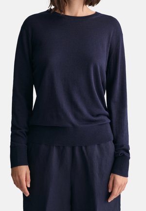 Kvinde iført en navyblå trøje med lange ærmer, ribstrikkede manchetter og kant, kombineret med matchende navyblå bukser.