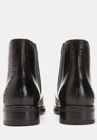 Czarne skórzane buty typu Chelsea z dekoracyjnym wzorem brogue, elastycznymi panelami po bokach i piętą na słupku. Gładkie wykończenie i zaokrąglony kształt czubka.