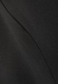 Tissu noir à côtes présentant des plis diagonaux, mettant en valeur une surface texturée avec de fines lignes. Matériau doux et flexible.