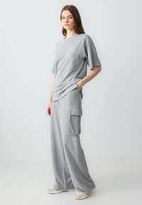 Graues Matching-Set mit einem locker sitzenden T-Shirt mit Brusttasche und weit geschnittenen Cargo-Hosen, beide aus weichem Stoff mit einer subtilen Textur.