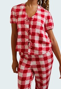 Red and pink checkered pajama set with heart patterns. Short-sleeve top features a V-neck and tie front; pants have a fitted design.