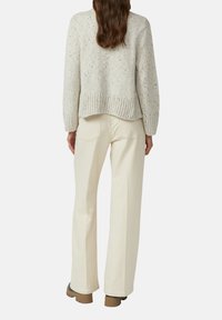 Chunky lichtgrijze gebreide trui met geribbelde zoom; gecombineerd met crèmekleurige high-waisted wijde broek en bruine laarzen. Gelaagde en casual look.