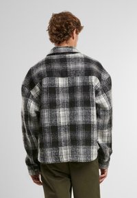 Svart og hvit rutete flanellskjorte med lange ermer, krage og rett hem, med teksturert stoff og store sjakkmønstre.