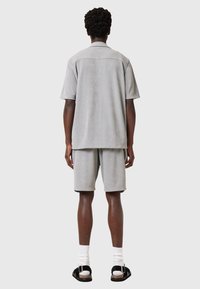 Grå tekstureret kortærmet skjorte parret med matchende shorts, begge lavet af blødt stof. Sorte sandaler komplementerer hvide sokker.