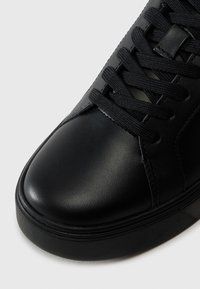 Zwarte leren sneaker met een ronde neus, een getextureerd oppervlak, zwarte veters en een platte zool met subtiele stikdetails.