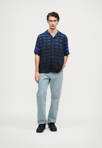 Tamsiai mėlynos spalvos trumpųjų rankovių marškiniai su tinklo raštu, derinami su šviesiai mėlynomis kelnėmis ir juodais batais. Marškiniai turi mygtukų užsegimą priekyje.