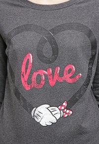 Maglietta grigia a maniche lunghe con una forma a cuore contornata di nero, con la scritta "amore" in rosa e un guanto bianco che tiene un fiocco a pois.