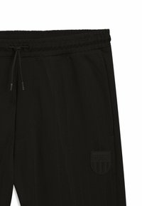 Schwarze, zulaufende Hose mit elastischem Bund und Kordelzug. Strukturierter Stoff mit gummiertem Logo-Patch. Klassisches Design mit Seitentaschen.