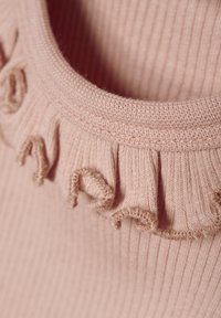Ljusrosa ribbad skjorta med en rund halsringning och en texturerad volangkant. Tyget verkar mjukt med en stretchig textur.