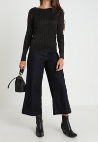 Svart ribbad långärmad tröja, vida byxor i mörk denim och ankle-length svarta stövlar. Liten svart väska med en dekorativ rem.