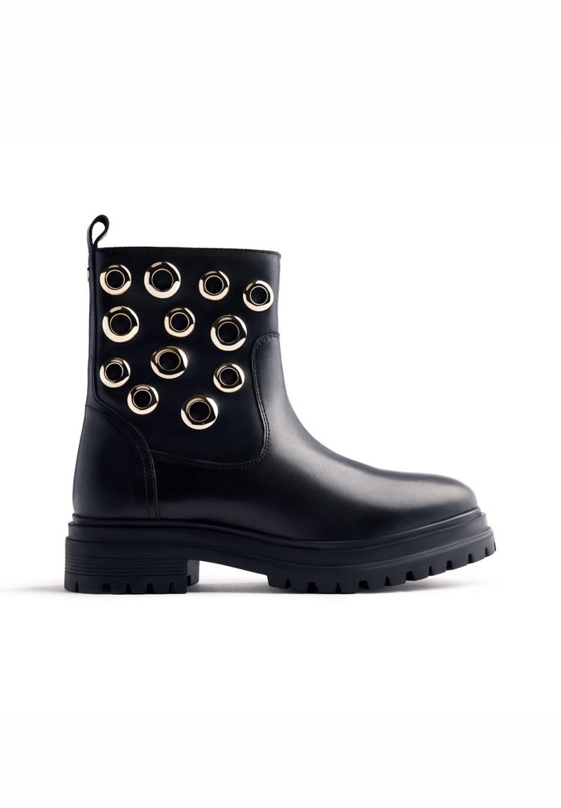 Bottine en cuir noir avec semelle épaisse et multiples grandes œillets en métal doré décorant le côté.