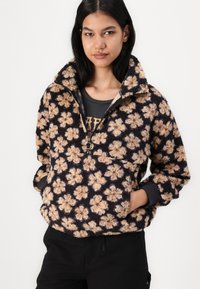 Chaqueta de forro polar negra con estampado floral, que presenta un cuello alto, cierre de cuarto de cremallera y puños elásticos, con una superficie suave y texturizada.