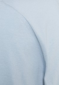 Tela de algodón azul claro con una textura suave, mostrando un primer plano de la costura del hombro y detalles ligeramente acanalados.