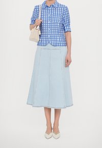 Camicia a quadri blu e bianchi con maniche corte, abbinata a una gonna A-line in denim chiaro. Una borsa beige e scarpe con punta completano l'outfit.