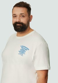 Witte katoenen T-shirt met blauwe bedrukte tekst "LAKESHORE RAFTING SCOUT" op de borst. Korte mouwen, ronde hals, ontspannen pasvorm.