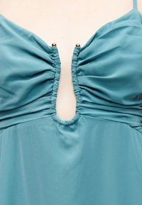 Μπλε αμάνικο ένδυμα με ρυτιδιασμένο ύφασμα, κεντρικό V-κομμένο ντεκολτέ και δύο ασημένιες διακοσμητικές μπάλες στις πάνω άκρες.