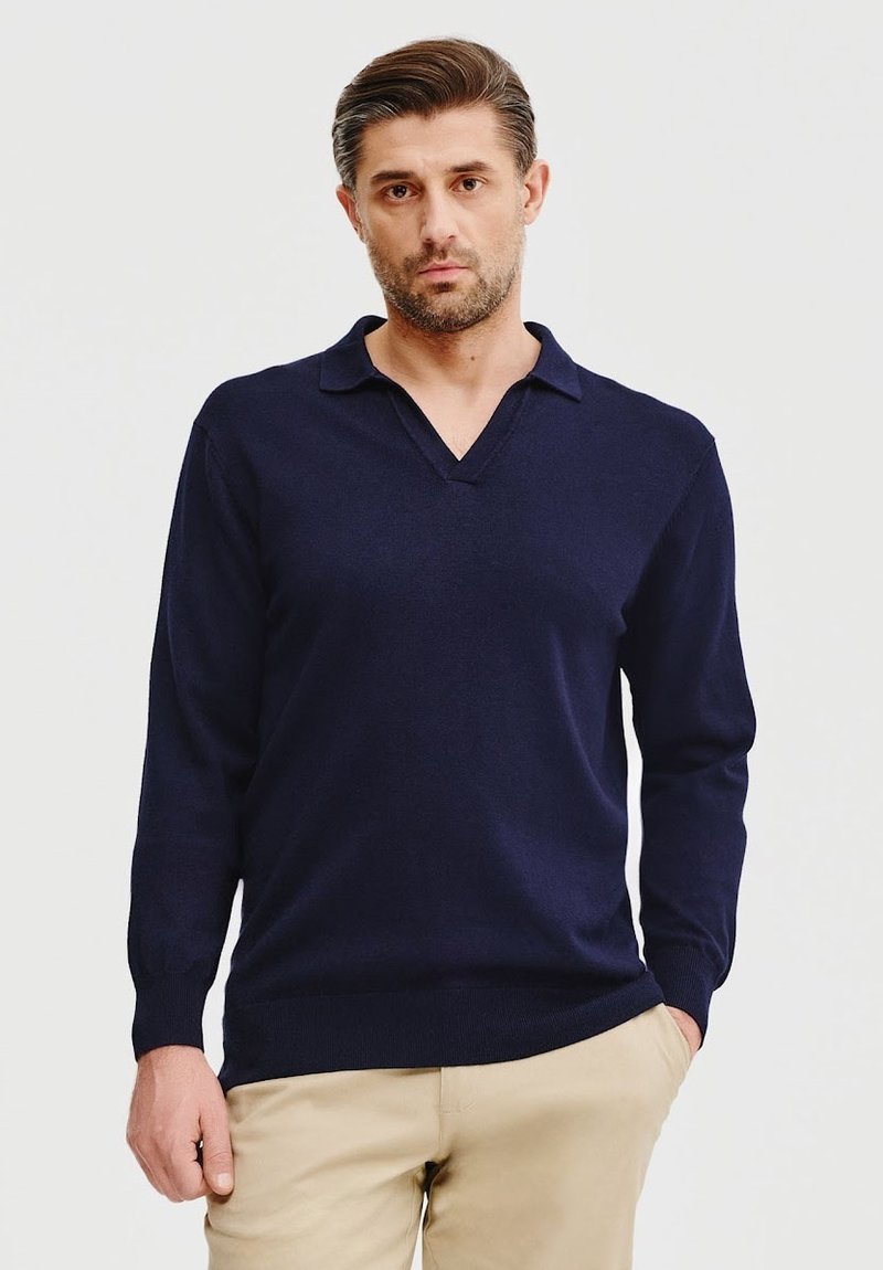 Granatowy sweter typu pullover z długim rękawem i dekoltem w kształcie litery V, o miękkiej fakturze, charakteryzujący się minimalistycznym wzornictwem oraz ściągaczami przy mankietach i u dołu.