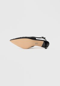 Pantof cu vârf ascuțit, negru, slingback, cu tocul mic de tip kitten și cu studuri decorative pe partea superioară, prezentat din partea tălpii pe un fundal alb.