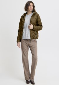 Alyvuogių žalios spalvos pūsta striukė su chevrono raštu, derinama su šviesiai pilku megztiniu ir smėlio spalvos kelnėmis. Tekstūruota medžiaga ir gobtuvo detalė.