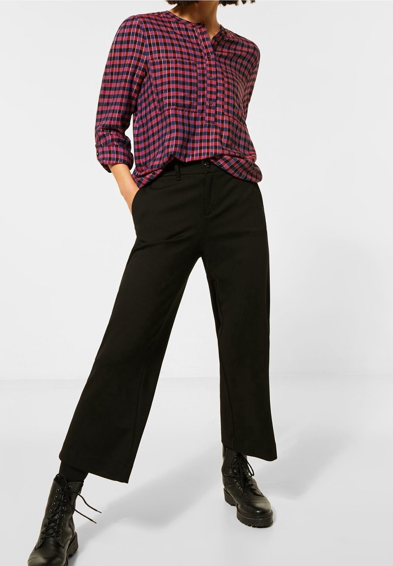 Chemise à carreaux boutonnée dans des tons rouges et bleus avec un col arrondi, associée à un pantalon noir taille haute et des bottes à lacets noires.