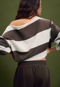 Felpa corta a righe marroni e grigie con maniche larghe, in tessuto misto cotone e design con spalle scoperte, abbinata a pantaloni scuri.