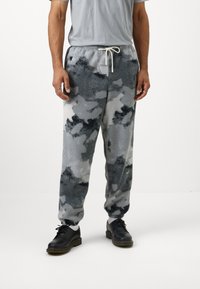 Szürke fleece melegítőnadrág fekete-fehér álcázó mintával. Rugalmas derékpánt állítható zsinórral; szűkített a bokánál.