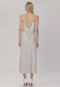 Robe midi à pois en blanc et noir, avec des bretelles fines, un dos nu avec fermeture à nouer, et une texture de tissu lisse.