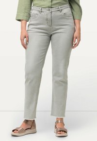 Jeans in denim grigio chiaro con taglio dritto, caratterizzati da tasche e orlo sfilacciato, abbinati a sandali con cinturini in bronzo su uno sfondo neutro.