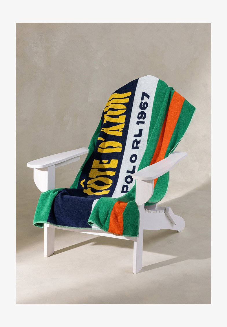 Chaise en bois blanche avec une serviette colorée surdimensionnée drapée dessus, présentant des motifs verts, bleu marine, orange et jaunes.