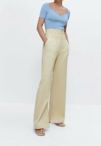 Modrý žebrovaný top s krátkým rukávem v kombinaci s béžovými kalhotami s vysokým pasem a širokými nohavicemi, které mají přední kapsy a hladkou texturu.