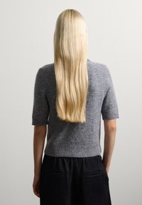 Grauer, kurzärmeliger Strickpullover mit weichem Textur, gerippten Bündchen und Saum, kombiniert mit schwarzen Hosen. Lange, glatte blonde Haare sichtbar.
