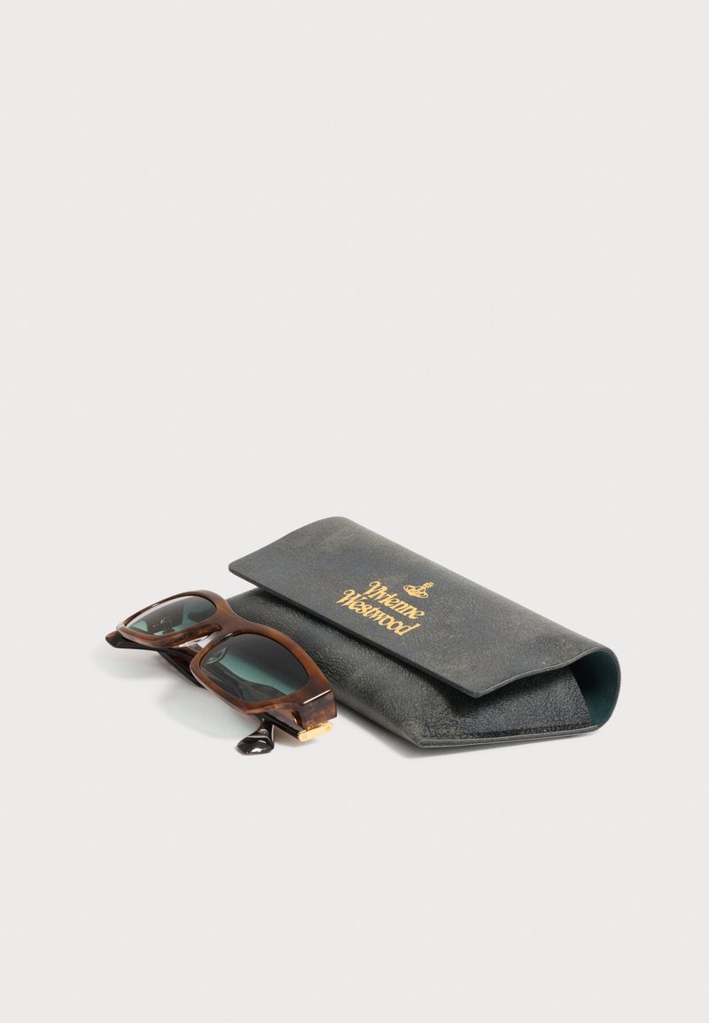 Brown tortoiseshell sunglasses with dark lenses next to a black leather Vivienne Westwood branded case on a white surface.