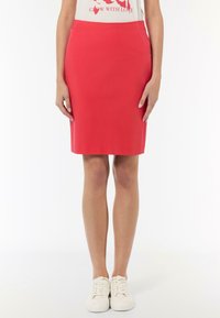 Roter Bleistiftrock mit glatter Textur und taillierter Passform. Verfügt über einen Taillenbund und seitliche Taschen, kombiniert mit weißen Sneakers.