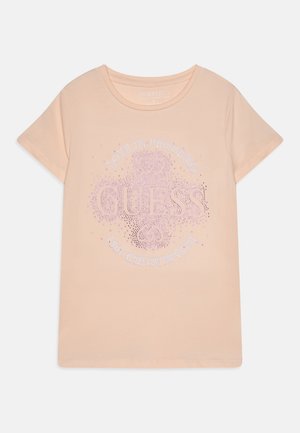Peach-colored cotton t-shirt, round neckline, short sleeves, features "GUESS" and "LOVE IN PROGRESS" embellishments in rhinestones.