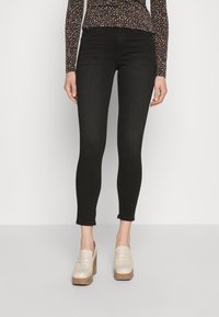 Vaqueros skinny negros con una textura suave y un ligero estiramiento. Combinados con mocasines de plataforma color crema. Se puede ver una blusa de manga larga con estampado.