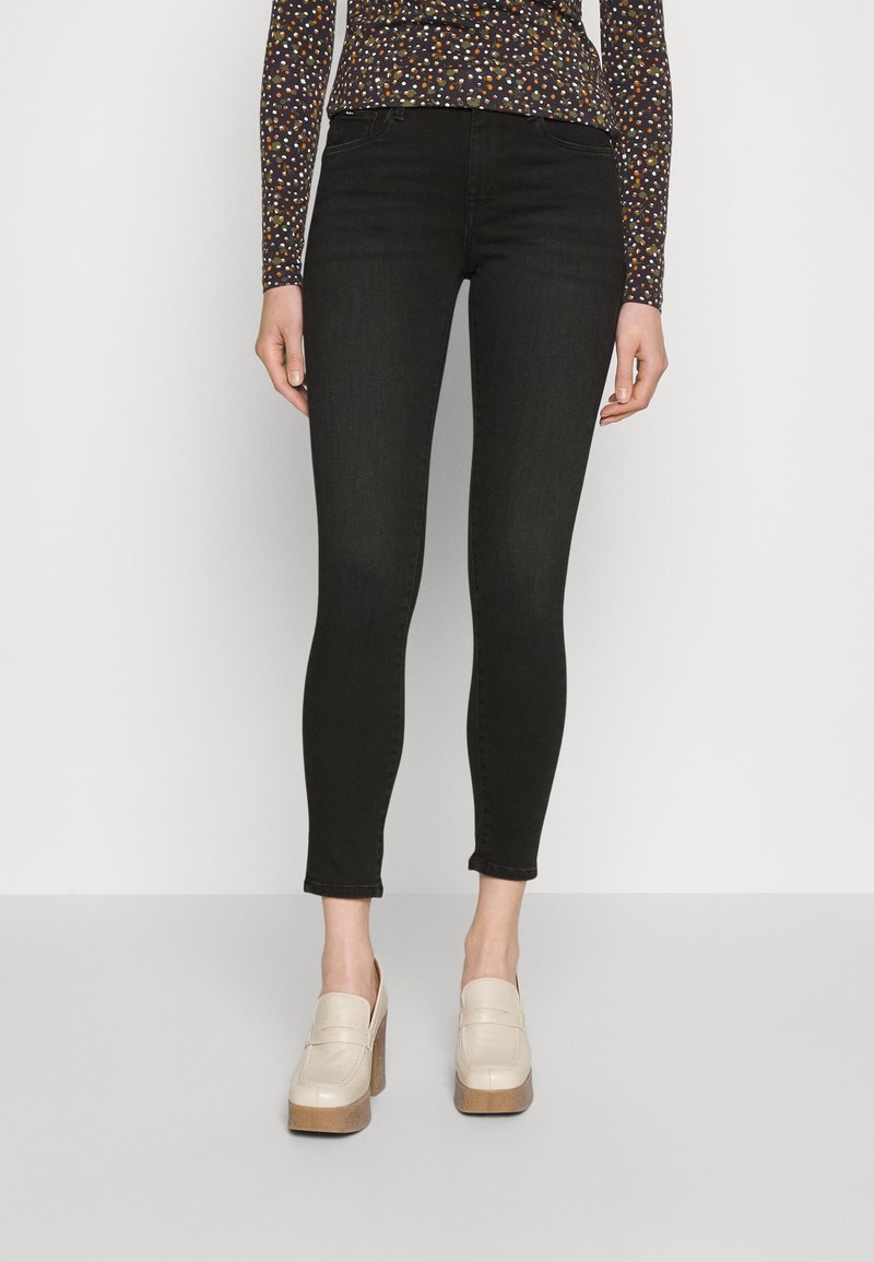 Vaqueros skinny negros con una textura suave y un ligero estiramiento. Combinados con mocasines de plataforma color crema. Se puede ver una blusa de manga larga con estampado.