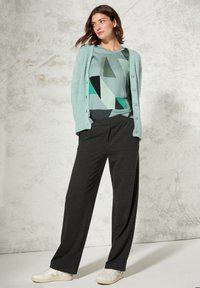 Miętowo-zielony kardigan z guzikami na geometrzycznym topie w kolorze teal, w połączeniu z ciemnoszarymi spodniami w szerokim kroju i białymi sneakersami.