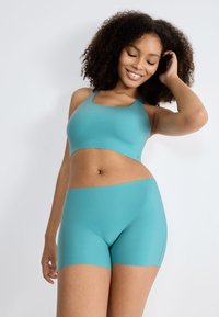 En turkise sportstop med firkantet halsudskæring, der er parret med matchende tætsiddende shorts, begge lavet af glat, strækbart stof.