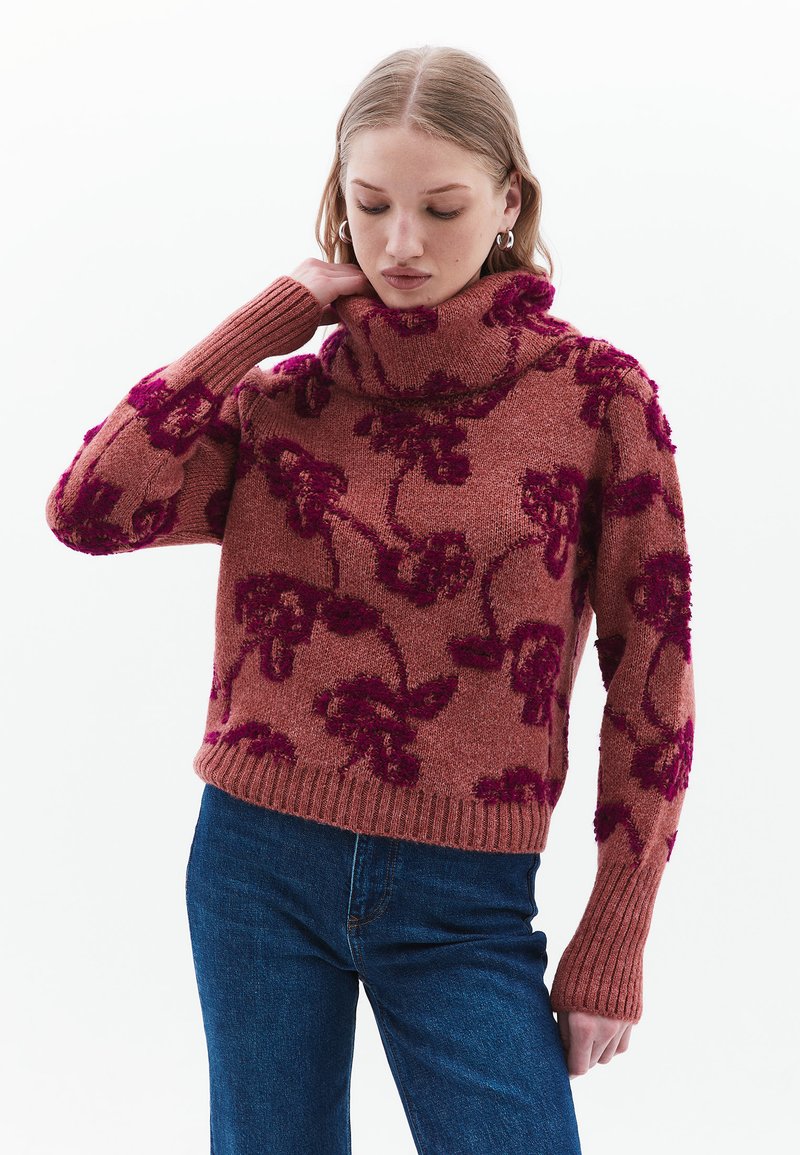 Gestrickter Pullover in Rostfarbe mit lila Blumenmuster, hoher Rollkragen, gerippte Bündchen und Saum, aus einem weichen Wollmischgewebe hergestellt.