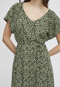 Black floral dress with short ruffled sleeves, v-neckline, and a tied waist. Features small green and white floral patterns across the fabric.