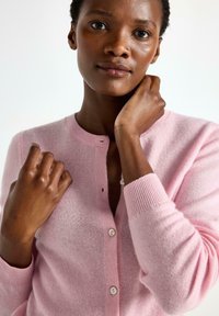 Lyserød cardigan lavet af blødt materiale, med rund halsudskæring, knaplukning og ribbede manchetter. Glat tekstur og enkelt design.