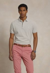 Ανοιχτού γκρι πόλο μπλούζα με γιακά, συνδυασμένη με ροζ chinos και πλεγμένη καφέ δερμάτινη ζώνη. Επίσης, είναι ορατό το αξιοσημείωτο πόρπη και ρολόι.