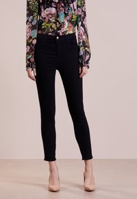 Pantalones vaqueros ajustados negros de tela elástica, con cintura alta, diseño de cinco bolsillos y un sutil detalle en el botón rosa.