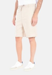 Pantaloni corti beige chiaro con una vestibilità rilassata, vita con cordoncino e tasche laterali. Il materiale sembra morbido. Abbinati a sneakers bianche.