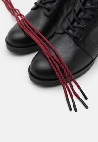 Bottes en cuir noir avec une finition texturée, dotées de lacets à motifs rouges et noirs et de semelles en caoutchouc à crampons prononcés.